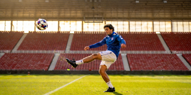 足球运动员在训练中练习任意球，背景是空旷的体育场